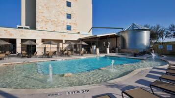 A swimming pool with lounge chairs and umbrellas, a building with stone facade, and a silo structure.