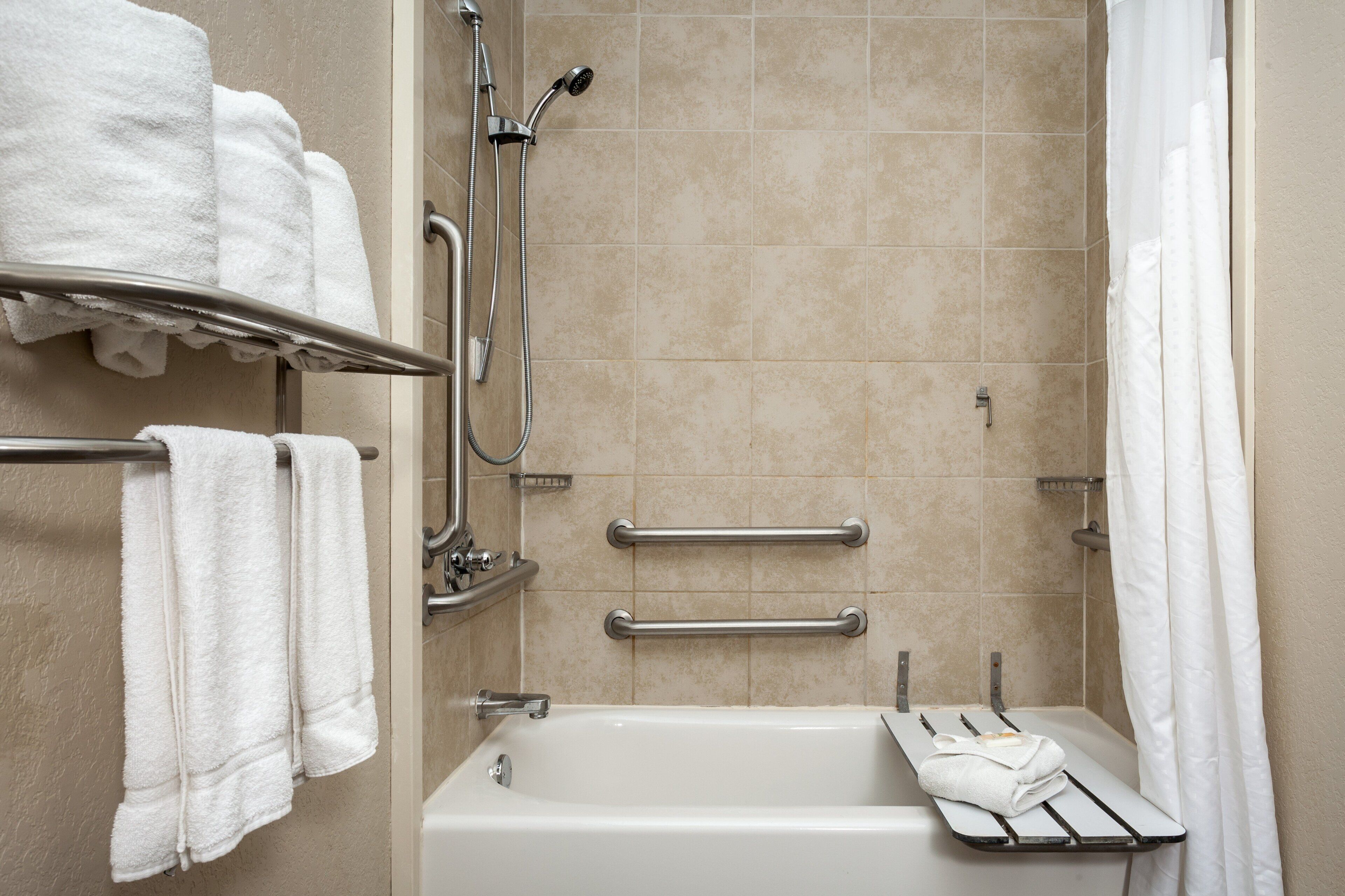 A modern bathroom with a bathtub, a shower with a handheld showerhead, and two grab bars.