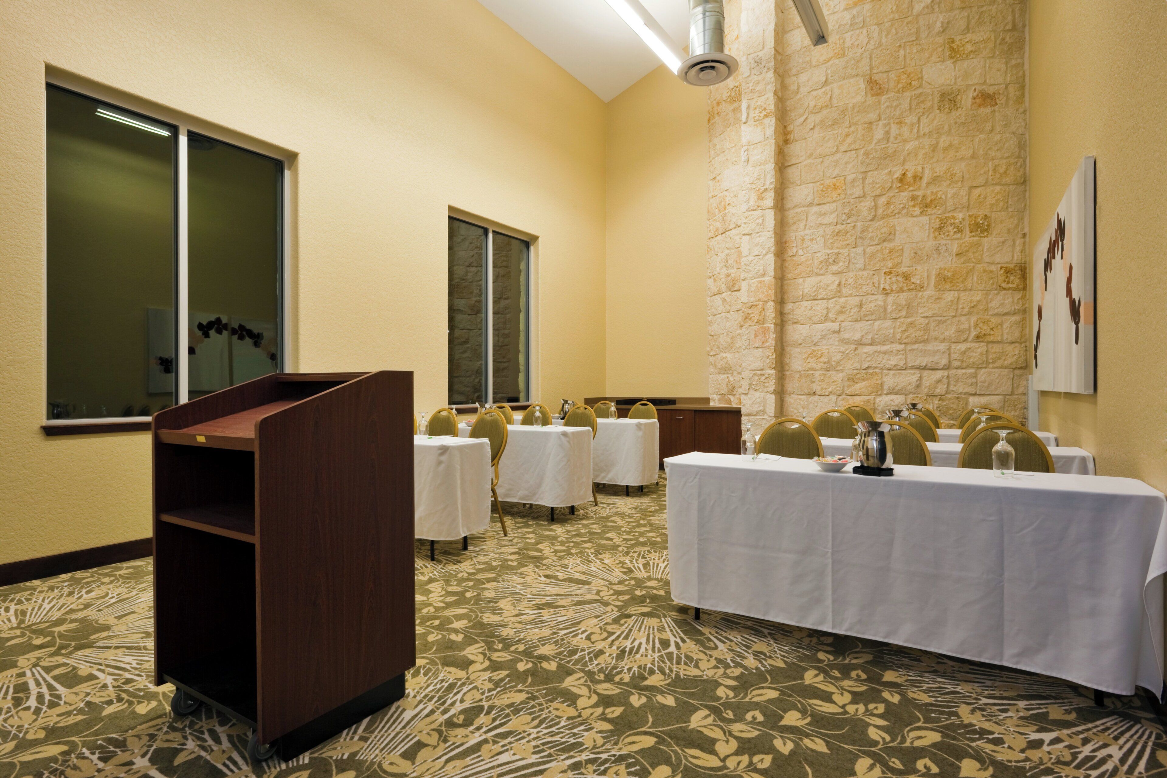 A conference room with tables and chairs, a podium, and a stone wall.