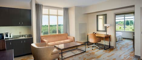 Ein modernes Hotelzimmer mit Sofa, Couchtisch, Schreibtisch und Blick auf Grünflächen.