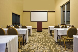 A conference room with tables and chairs, a projector screen, and a carpeted floor.