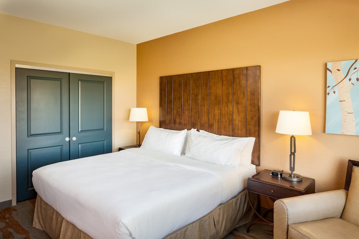 A hotel room with a large bed, two bedside tables with lamps, a wooden headboard, and a door.