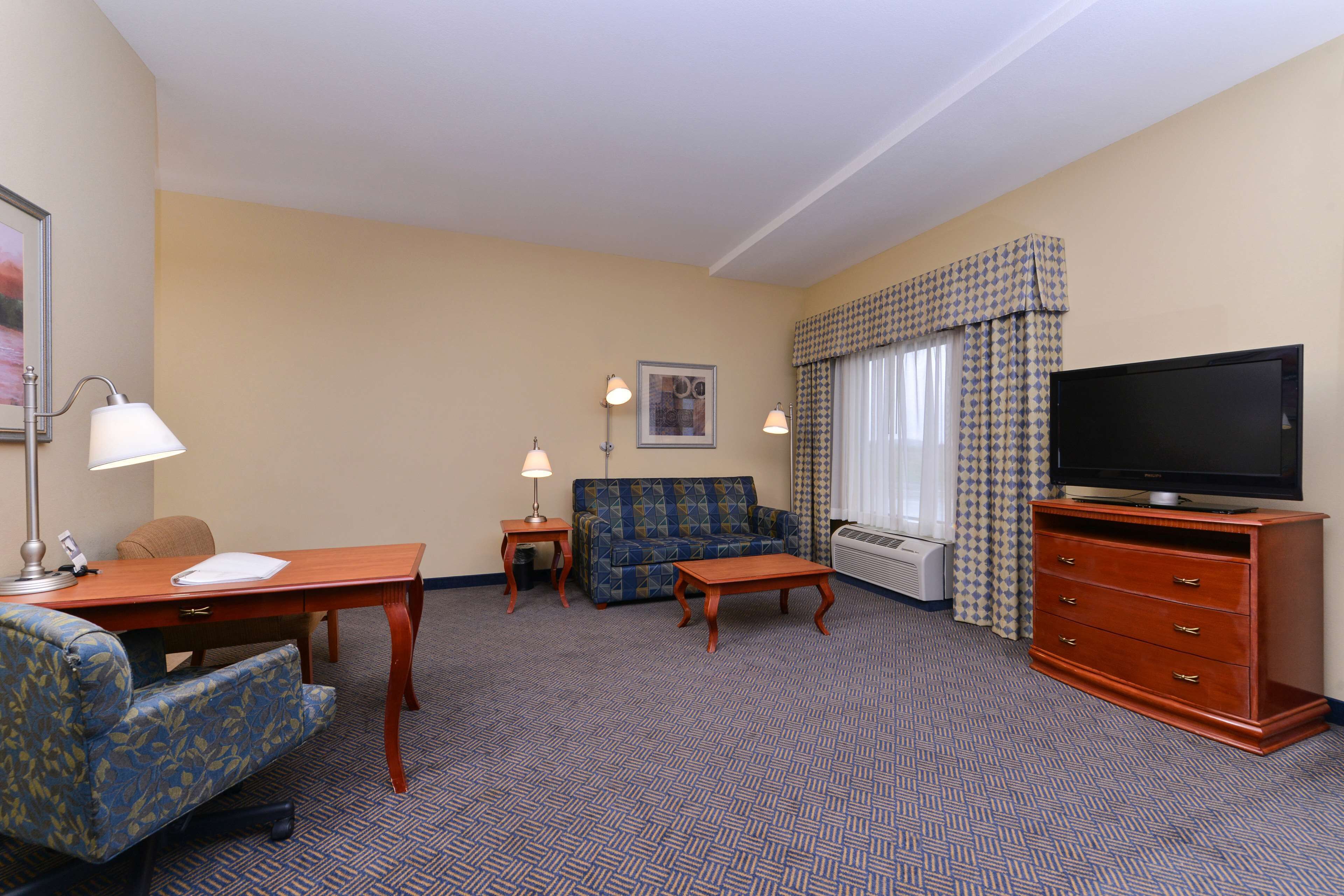 A hotel room with a sofa, a desk with a lamp, a television on a wooden cabinet, and a patterned carpet.