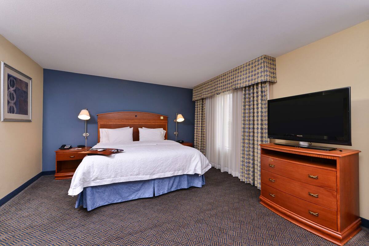 Une chambre d’hôtel avec un grand lit, une commode en bois, un téléviseur à écran plat et une table de chevet avec une lampe.
