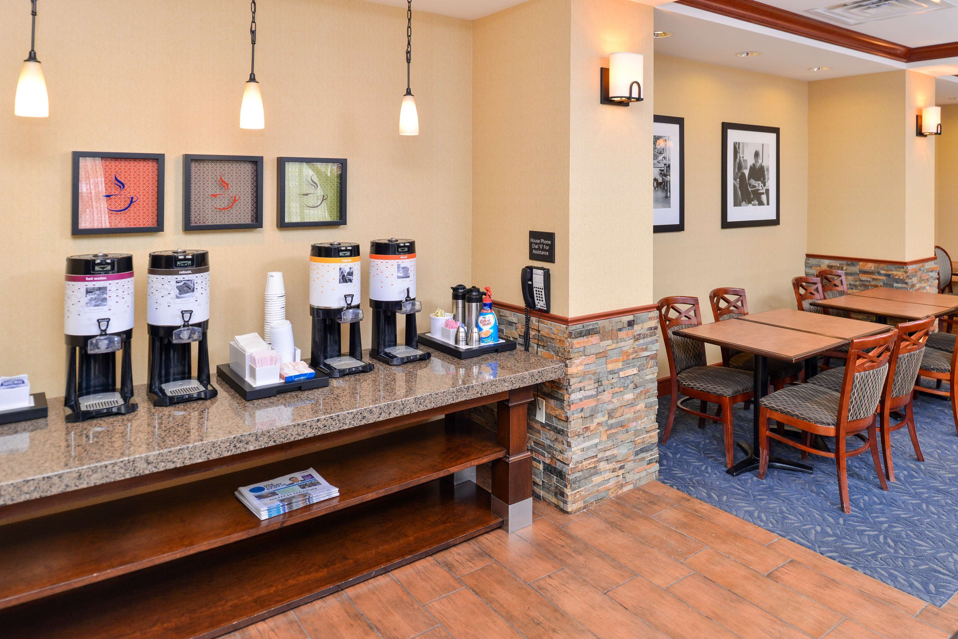 A hotel reception area with a coffee station, seating, and framed pictures on the wall.
