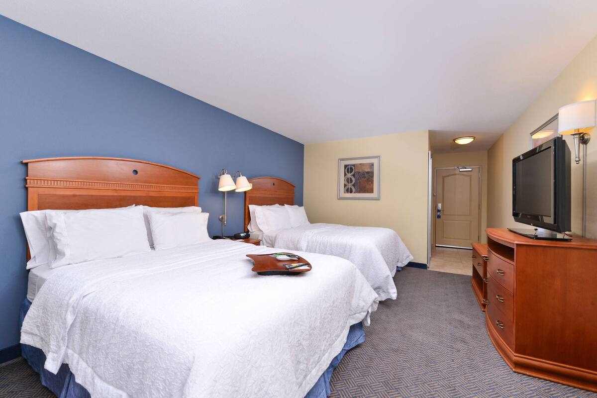 Une chambre d’hôtel avec deux lits, une télévision, une commode en bois et une porte donnant sur une autre pièce.