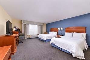 A hotel room with two beds, a desk, a television, and a chair.