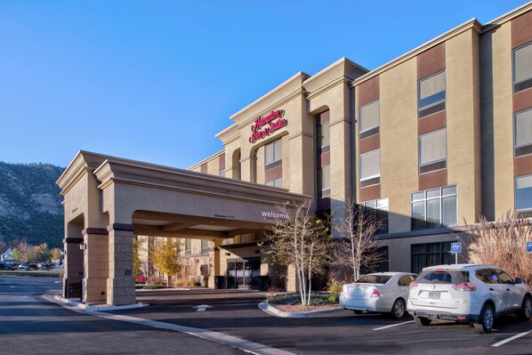 A hotel entrance with a clear sign, a covered driveway, and two parked cars.