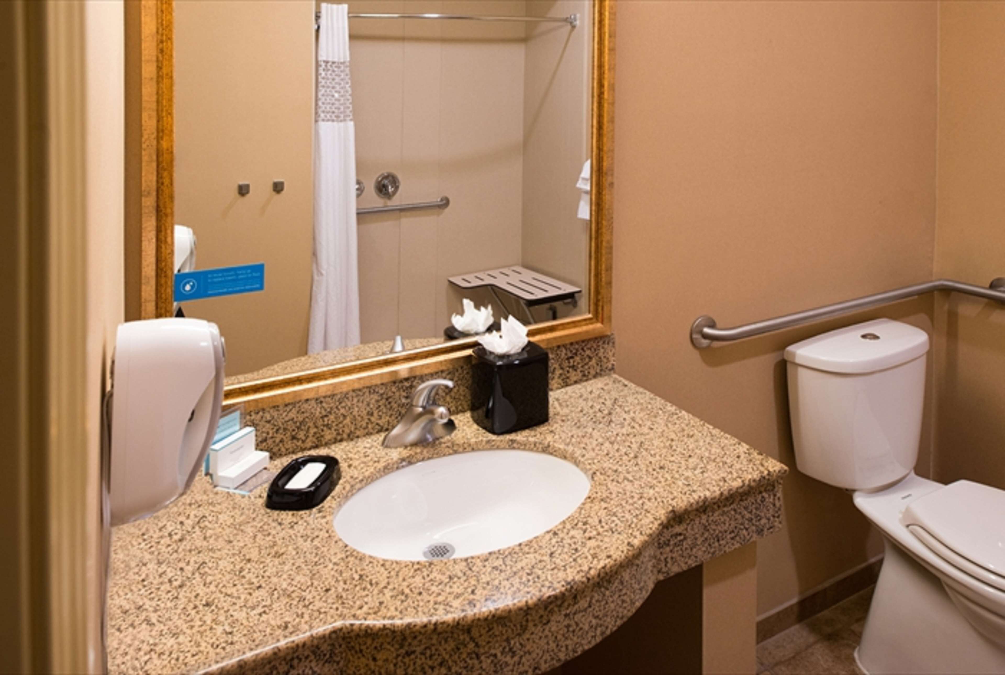 A bathroom with a granite countertop sink, a mirror, a hand dryer, a toilet, and a shower stall.