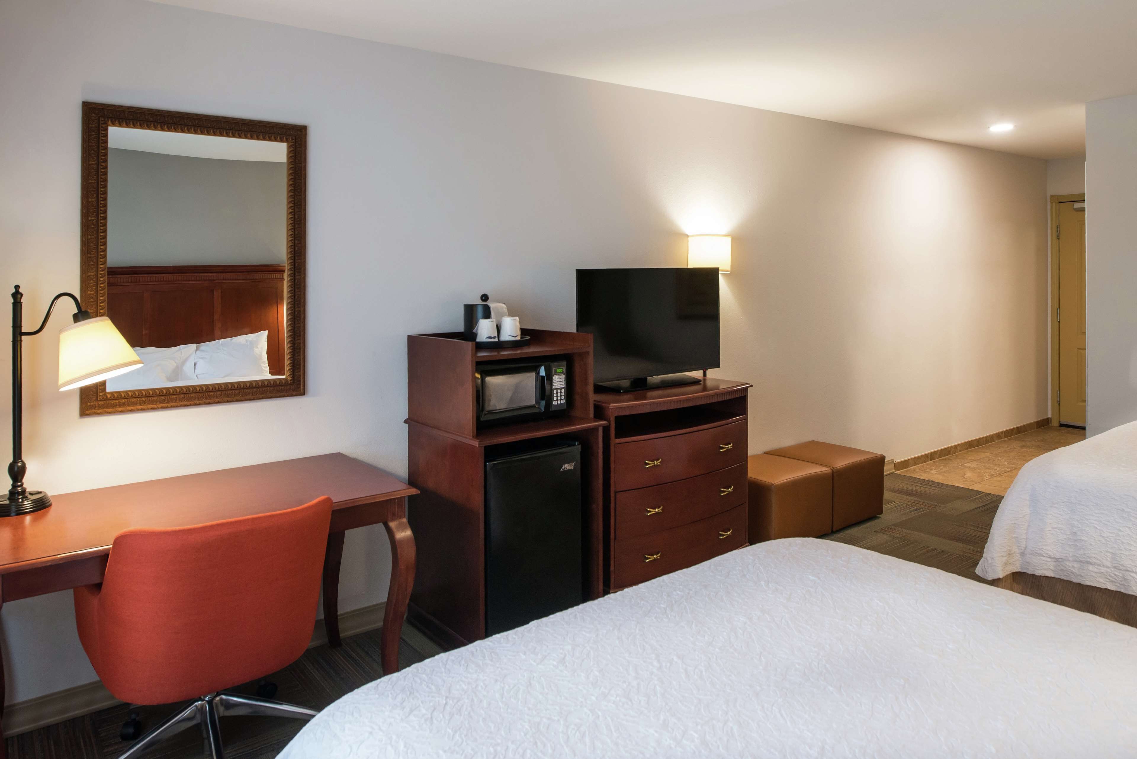 Habitación de hotel con cama, escritorio con silla, televisor, microondas, lámpara y cómoda.