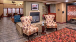 A lobby with two patterned armchairs, a fireplace, a dining area, and a carpeted floor.