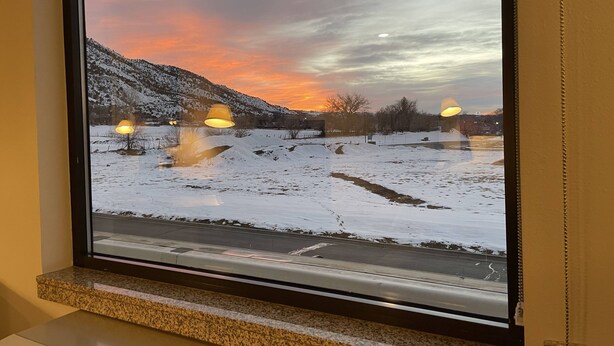 A window with a view of a snowy landscape during sunset.