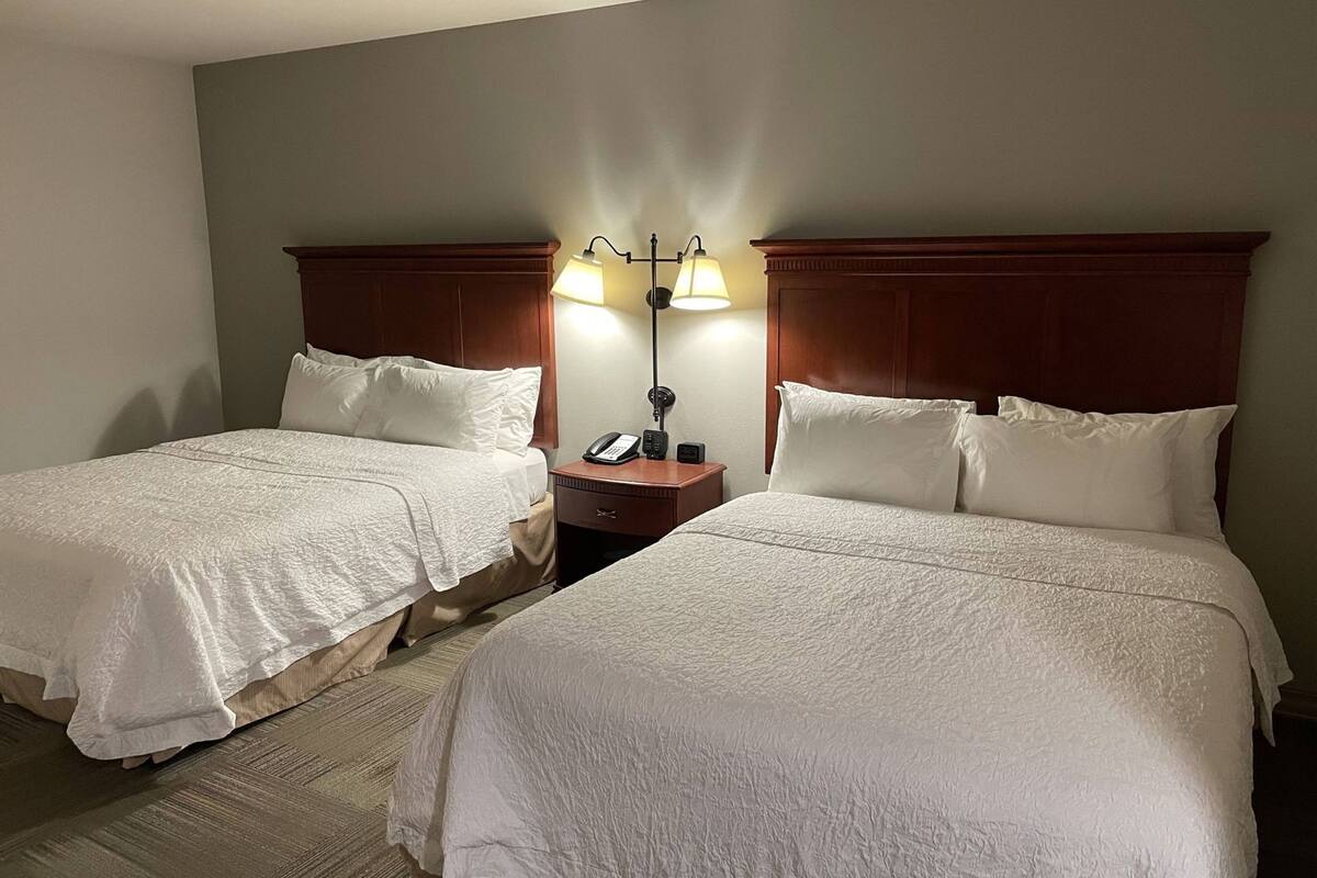 Quarto de hotel com duas camas, uma mesa de cabeceira com abajur e um telefone.