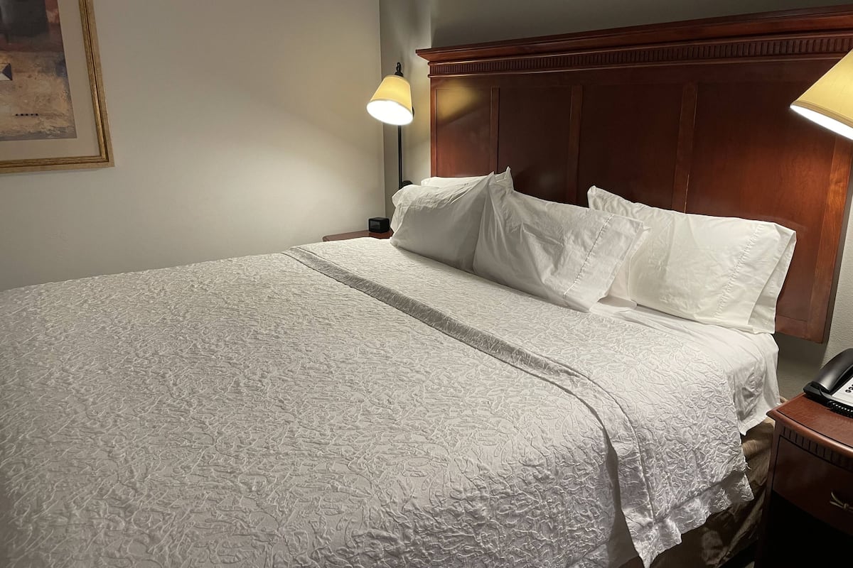 Uma cama bem arrumada com um edredom branco texturizado, uma cabeceira de madeira e duas luminárias laterais.