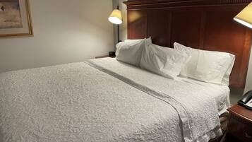 Una cama bien tendida con un edredón blanco texturizado, un cabecero de madera y dos lámparas de noche.