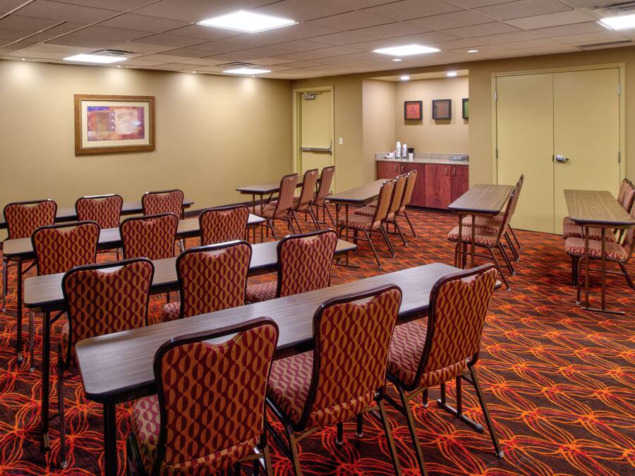 Un salón de conferencias con varias mesas y sillas, una kitchenette y una puerta que da a otra sala.