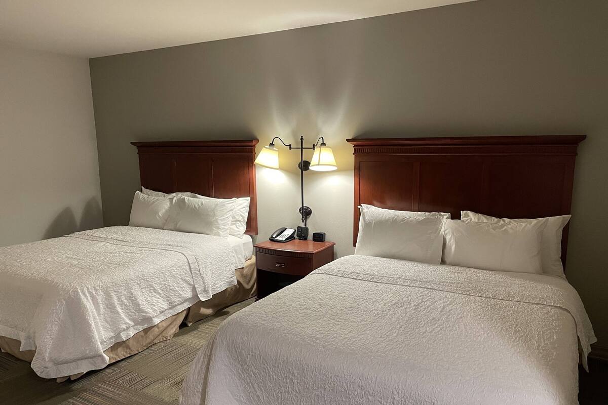 Quarto de hotel com duas camas, uma mesa de cabeceira com abajur e um telefone.
