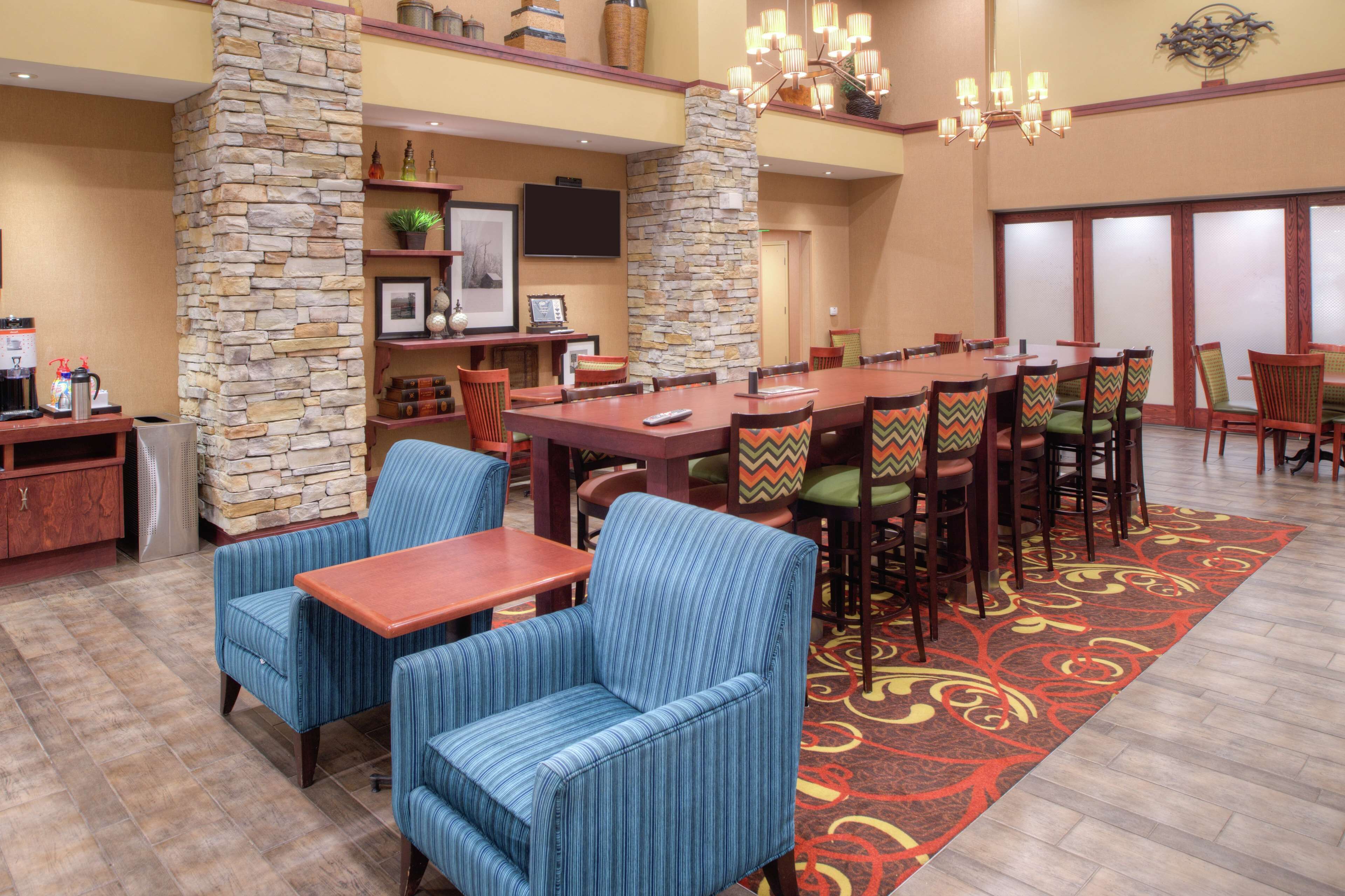 A hotel dining area with a stone pillar, striped chairs, a wooden table, and a television on the wall.