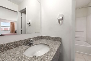 A bathroom with a granite countertop sink, a mirror, and a wall-mounted hair dryer.