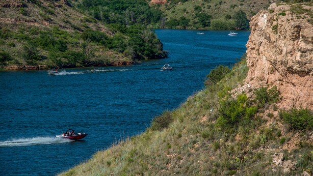 Un fiume con barche, circondato da colline verdi e scogliere rocciose.