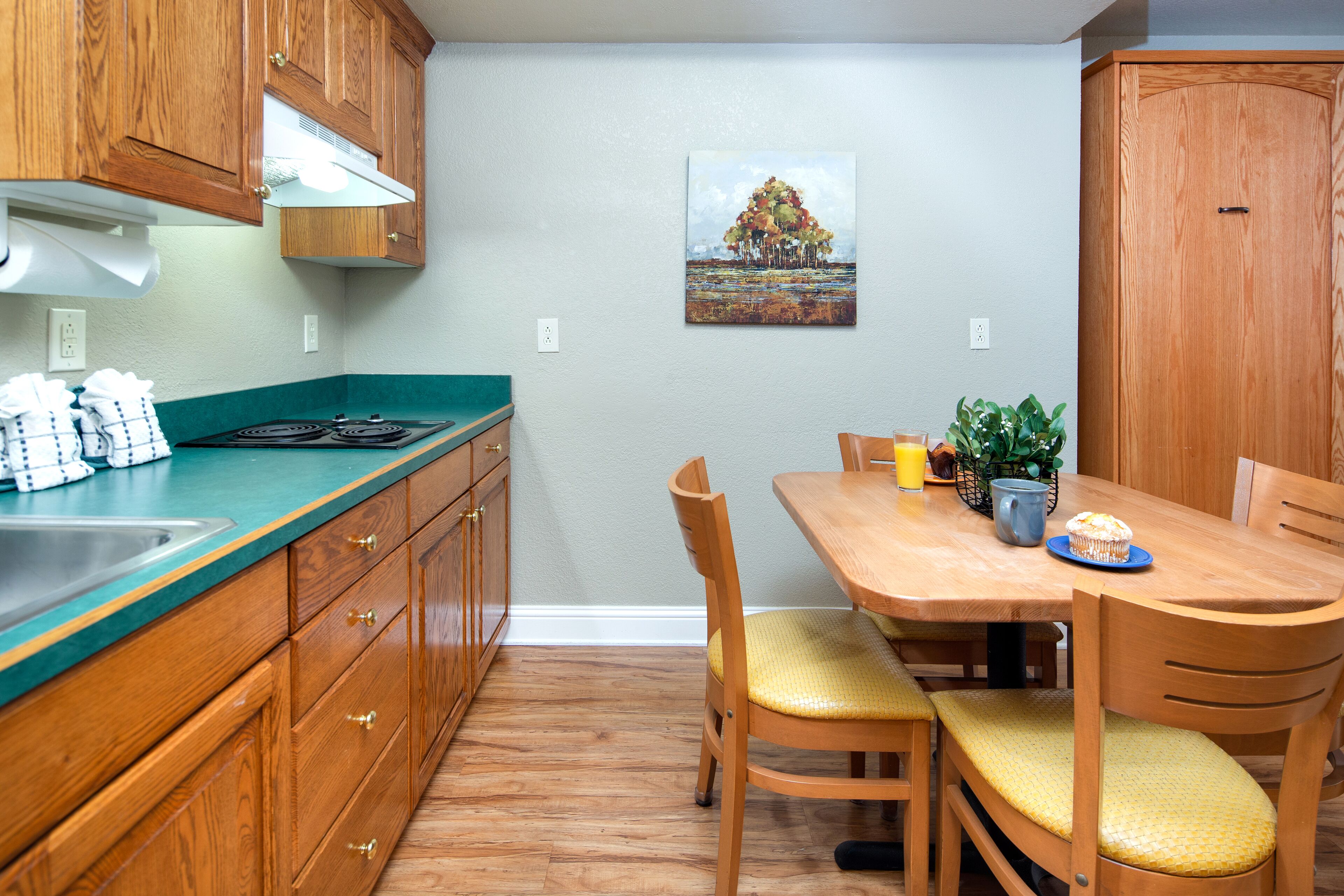 A kitchen with wooden cabinets, a teal countertop, and a dining table with chairs.