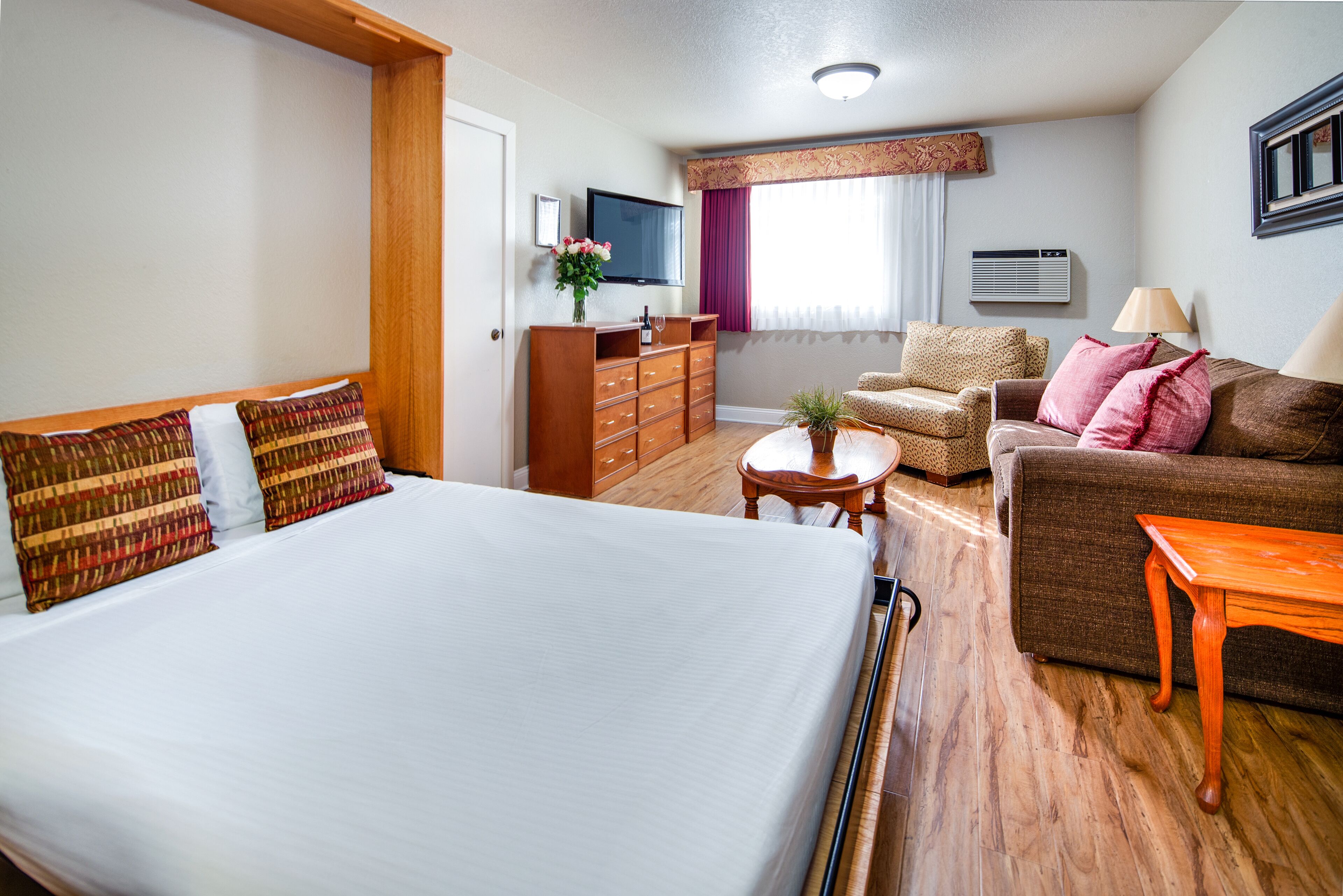 A hotel room with a large bed, a wooden dresser, a sofa, a small table, and a television.