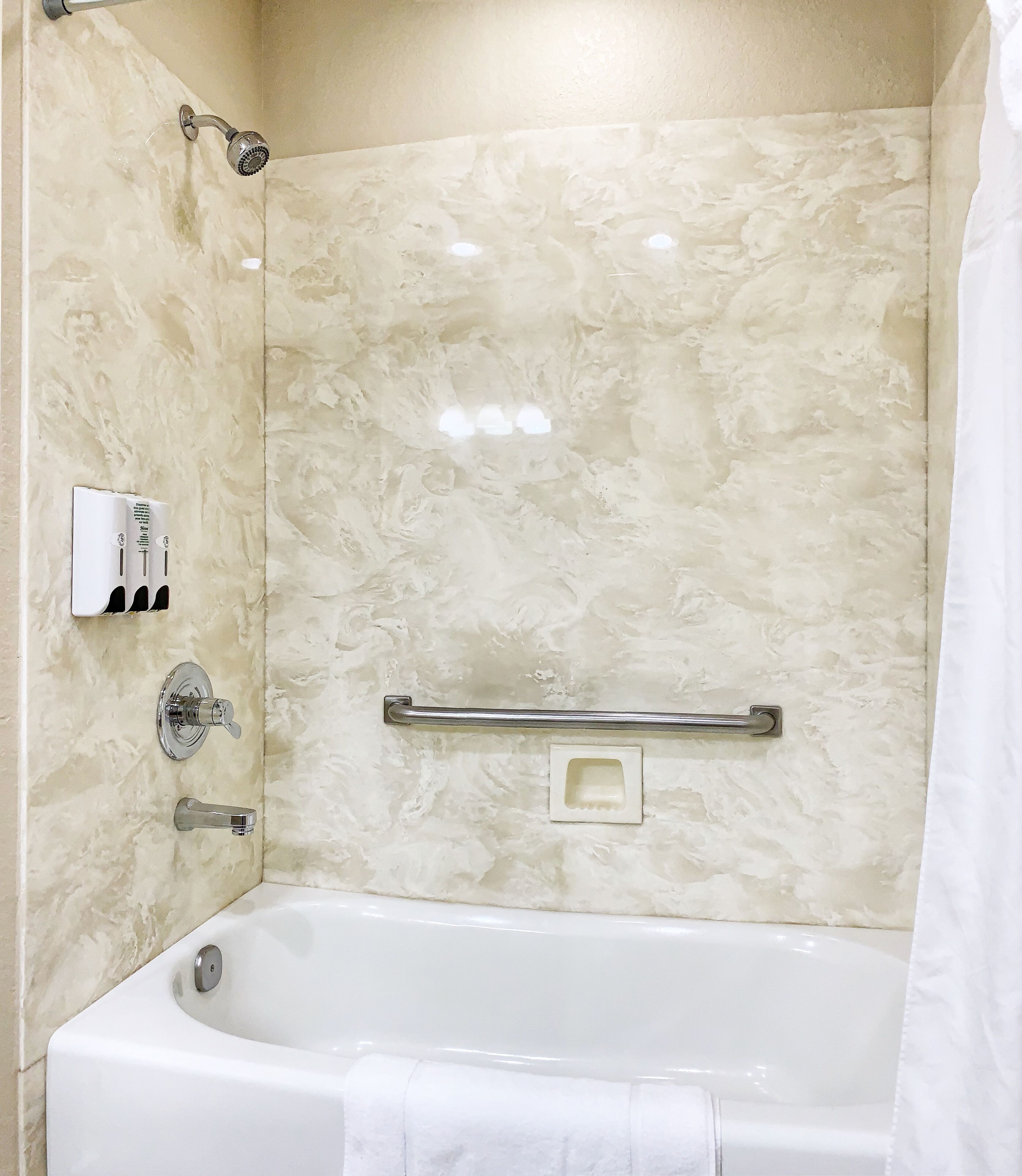 A bathroom with a bathtub, a showerhead, a hand dryer, and a soap dispenser.
