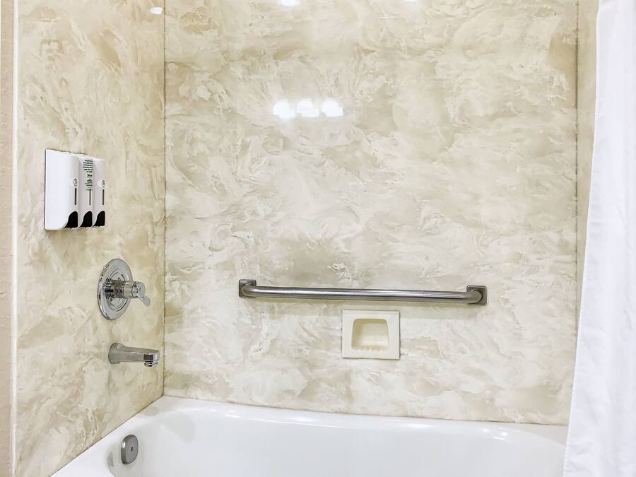 A bathroom with a bathtub, a showerhead, a hand dryer, and a soap dispenser.