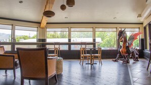 Un restaurante con sillas y mesas de madera, ventanas amplias y una escultura de dragón.