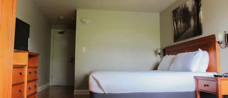 A hotel room with a bed, a wooden dresser, a television, and a painting on the wall.