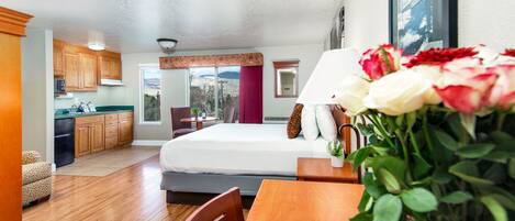 A compact hotel room with a kitchenette, a bed, a dining table, and a view of the outdoors.