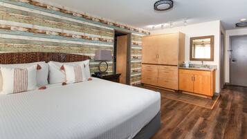 Une chambre avec un grand lit, une armoire en bois et une salle de bain équipée d’un miroir et d’un lavabo.