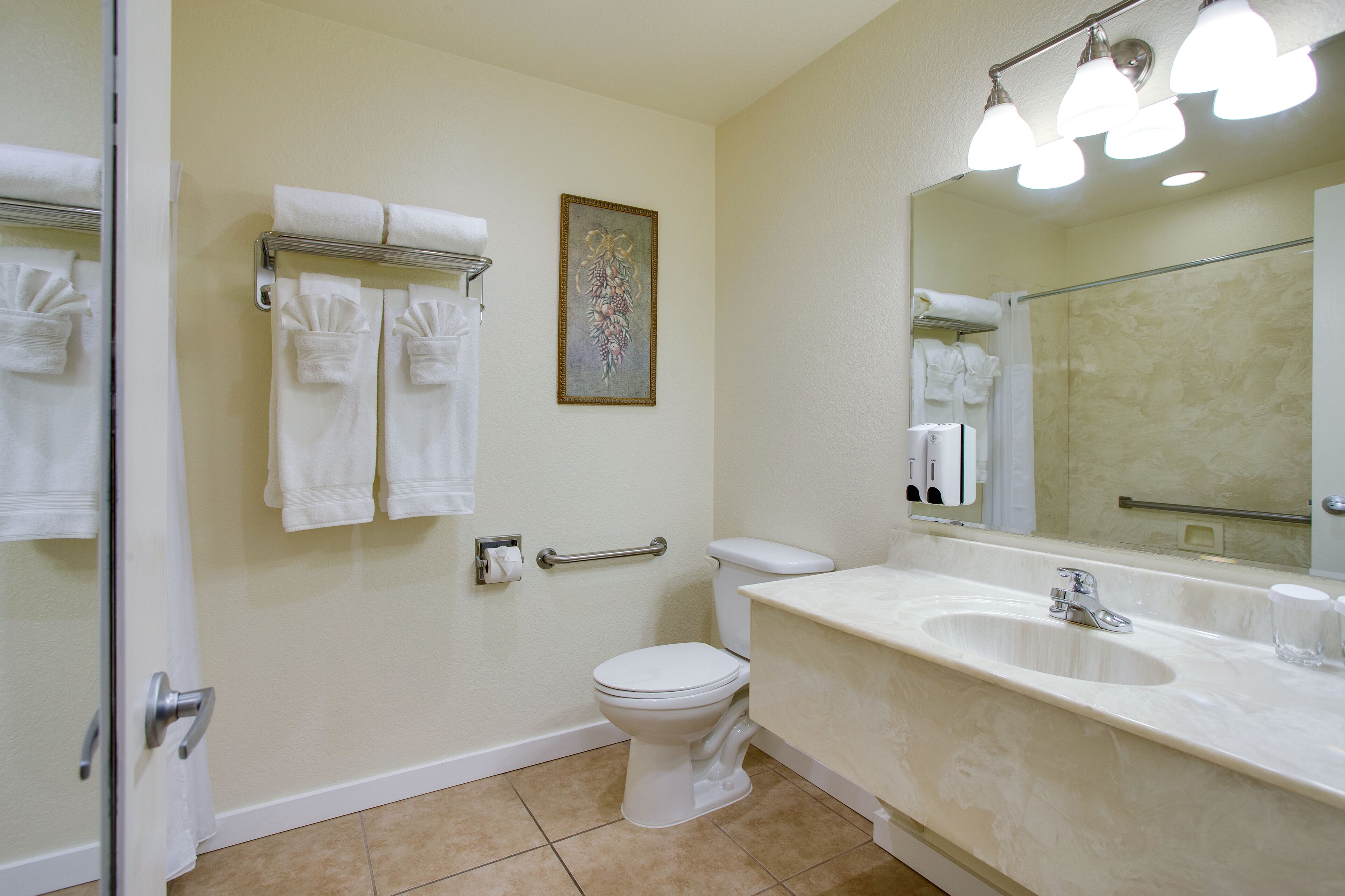 A bathroom with a toilet, sink, and a mirror. There are towels hanging on a rack and a framed picture on the wall.