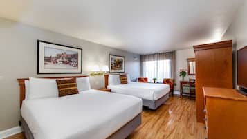A hotel room with two beds, a desk, a chair, a TV, and framed pictures on the wall.
