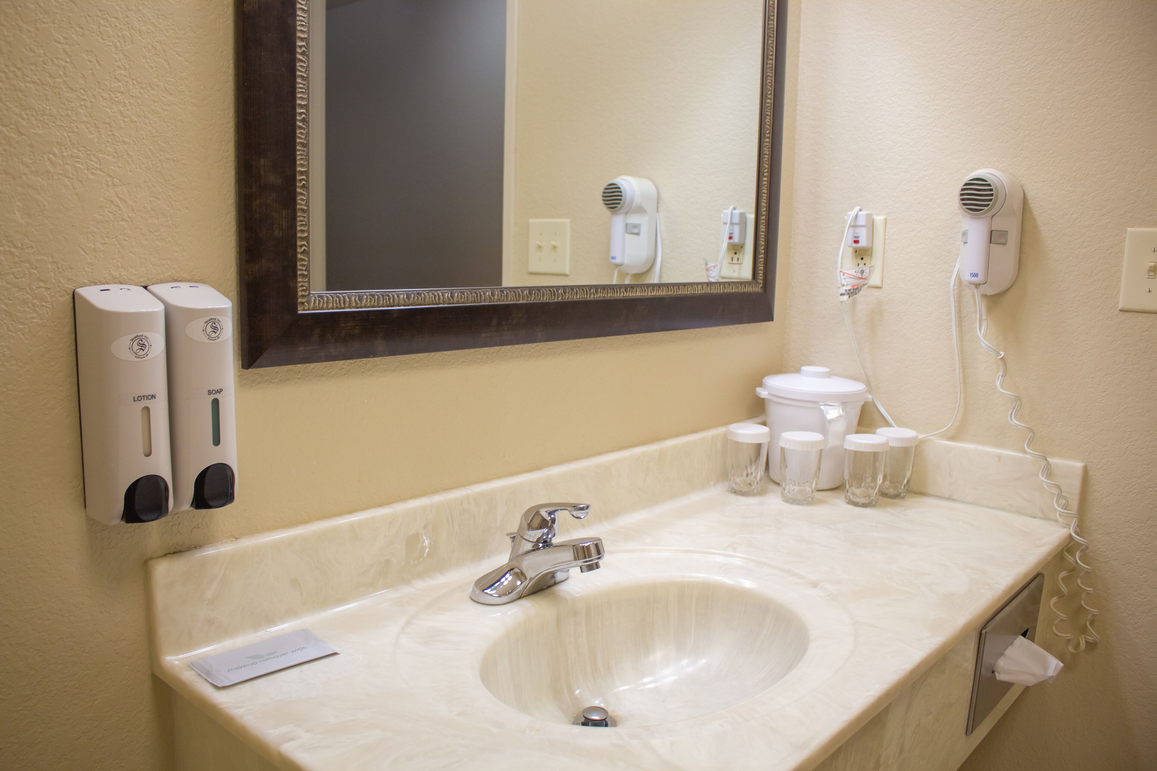 A hotel bathroom with a sink, mirror, and two hand dryers.