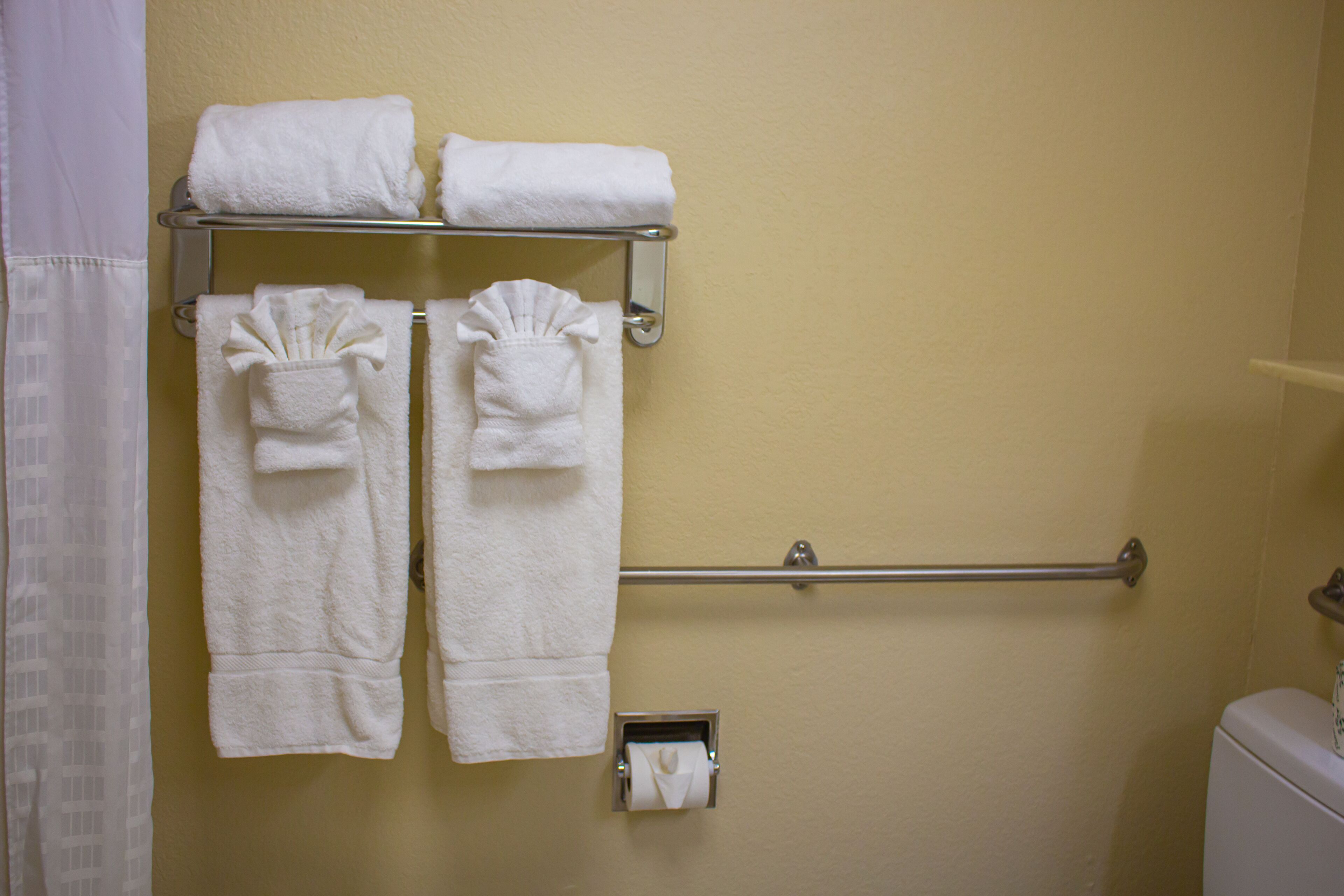 A bathroom with a towel rack holding several folded towels, a toilet paper holder, and a grab bar on the wall.