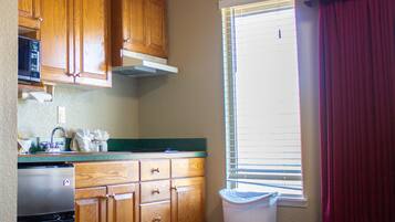 A kitchen with wooden cabinets, a stainless steel refrigerator, a microwave, and a window with blinds.