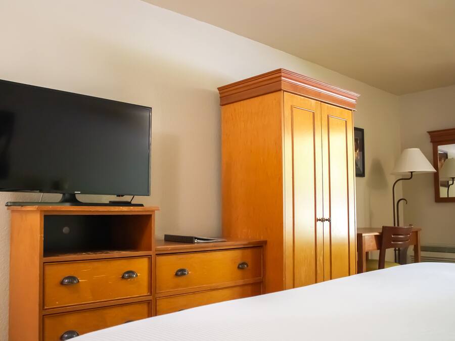 Habitación de hotel con cama, armario de madera, televisor, escritorio y silla, y una lámpara.