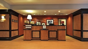 A reception area with a wooden reception desk, framed pictures, and a welcome sign. - Hampton Inn Defiance (Defiance)