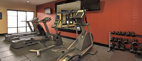 A hotel fitness center with treadmills, an elliptical, a rowing machine, and a rack of dumbbells.