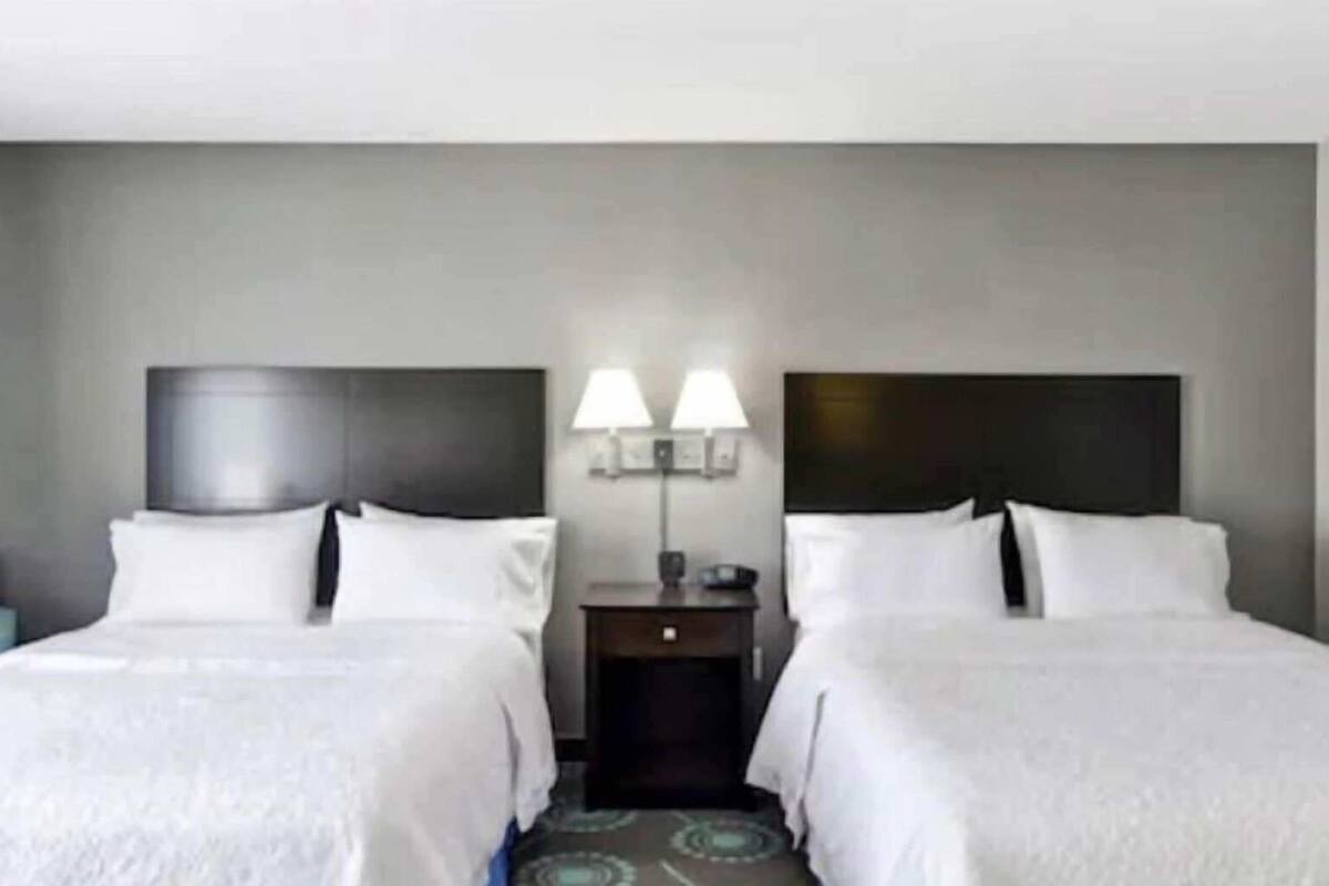 A hotel room with two beds, a nightstand with lamps, and a blue chair.
