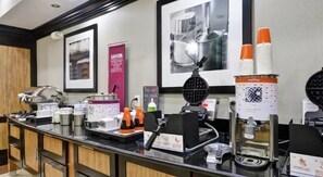 A self-service beverage station with multiple dispensers, including a waffle maker, and a menu board.