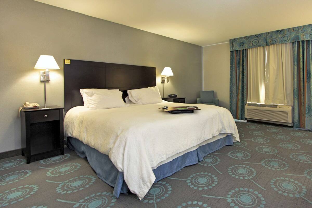 A hotel room with a large bed, two bedside tables with lamps, a chair, and a window with curtains.