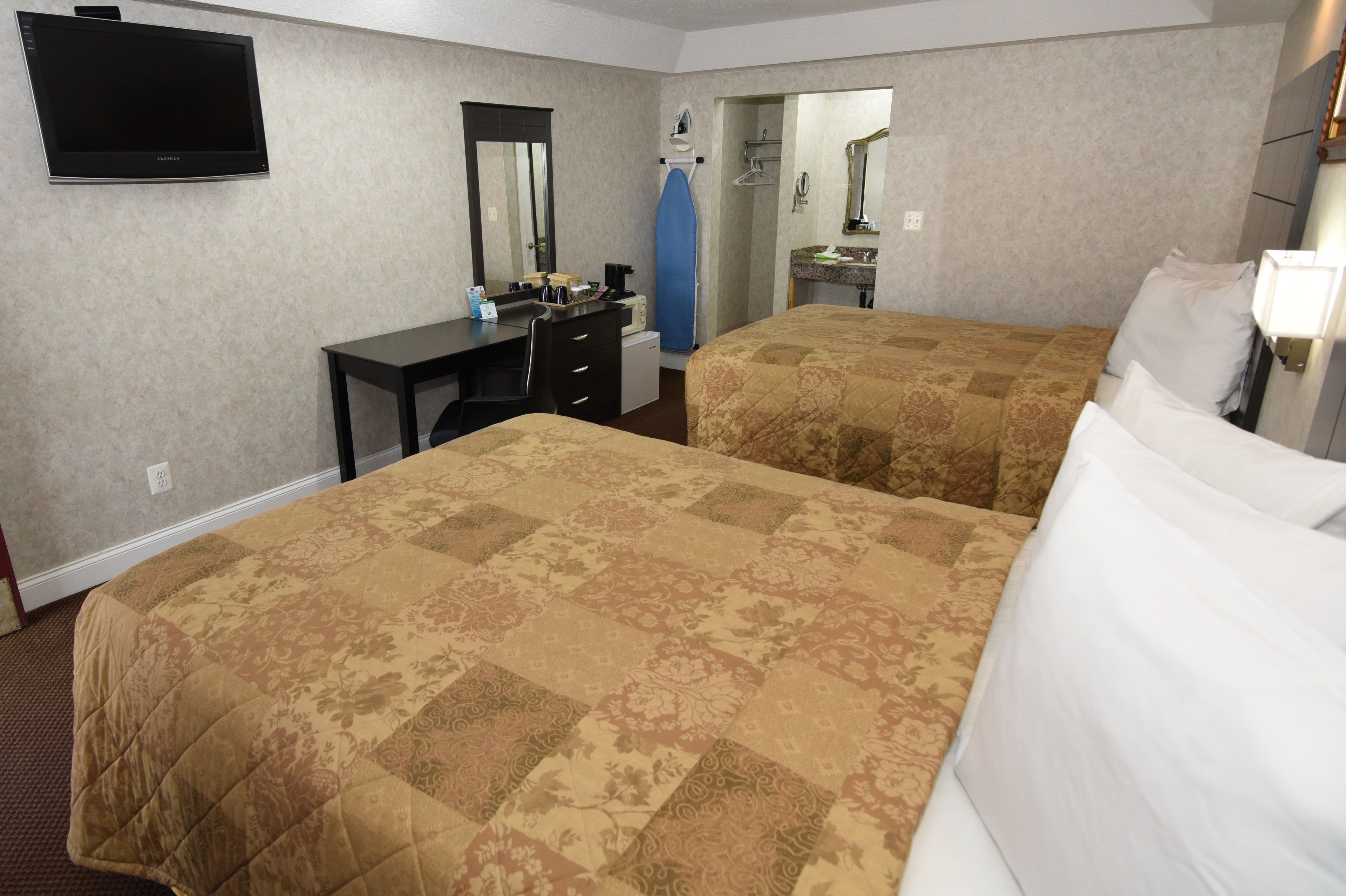 A hotel room with two beds, a desk, a television, and a mirror.