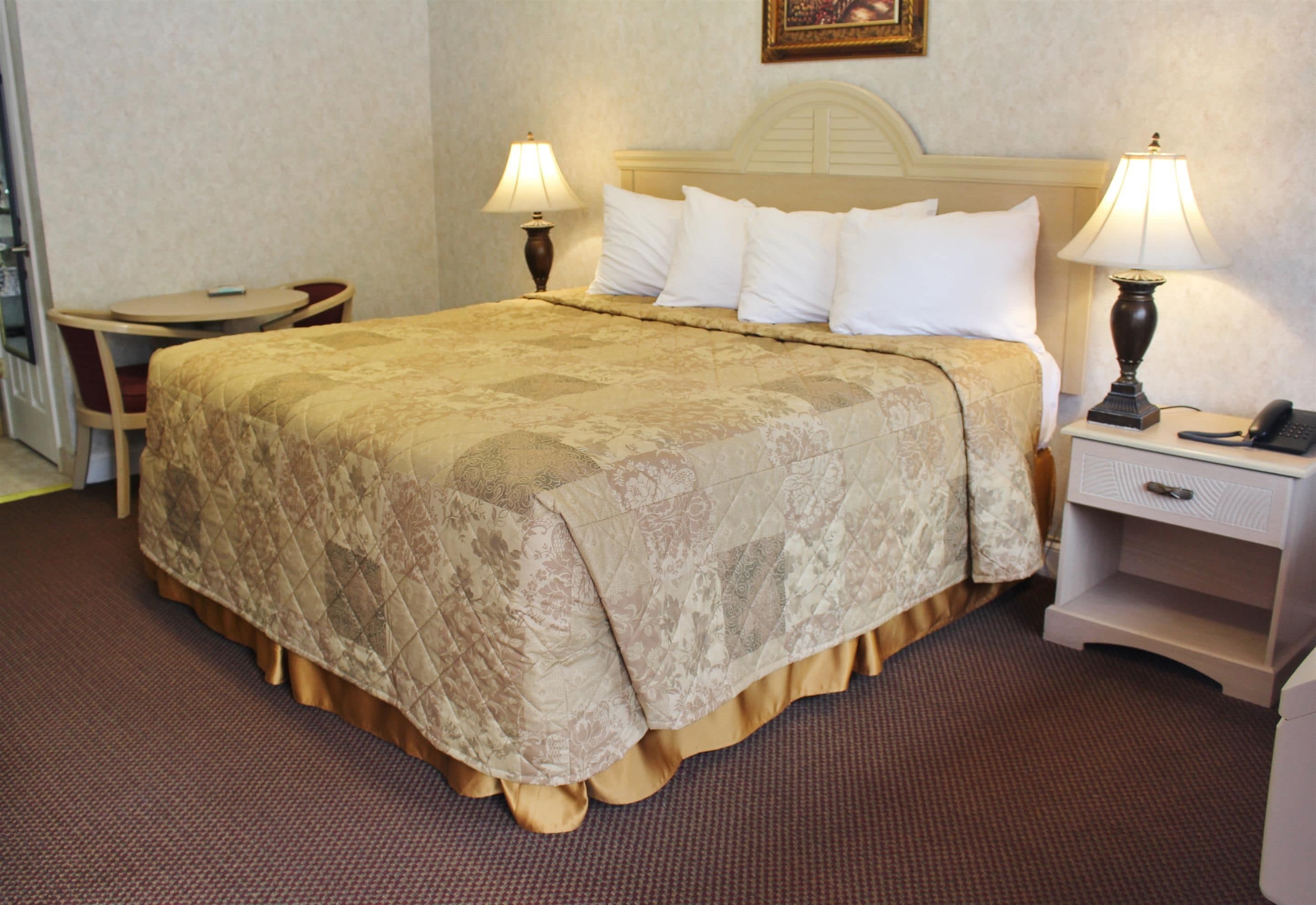 A hotel room with a large bed, two bedside tables with lamps, a small round table, and a chair.