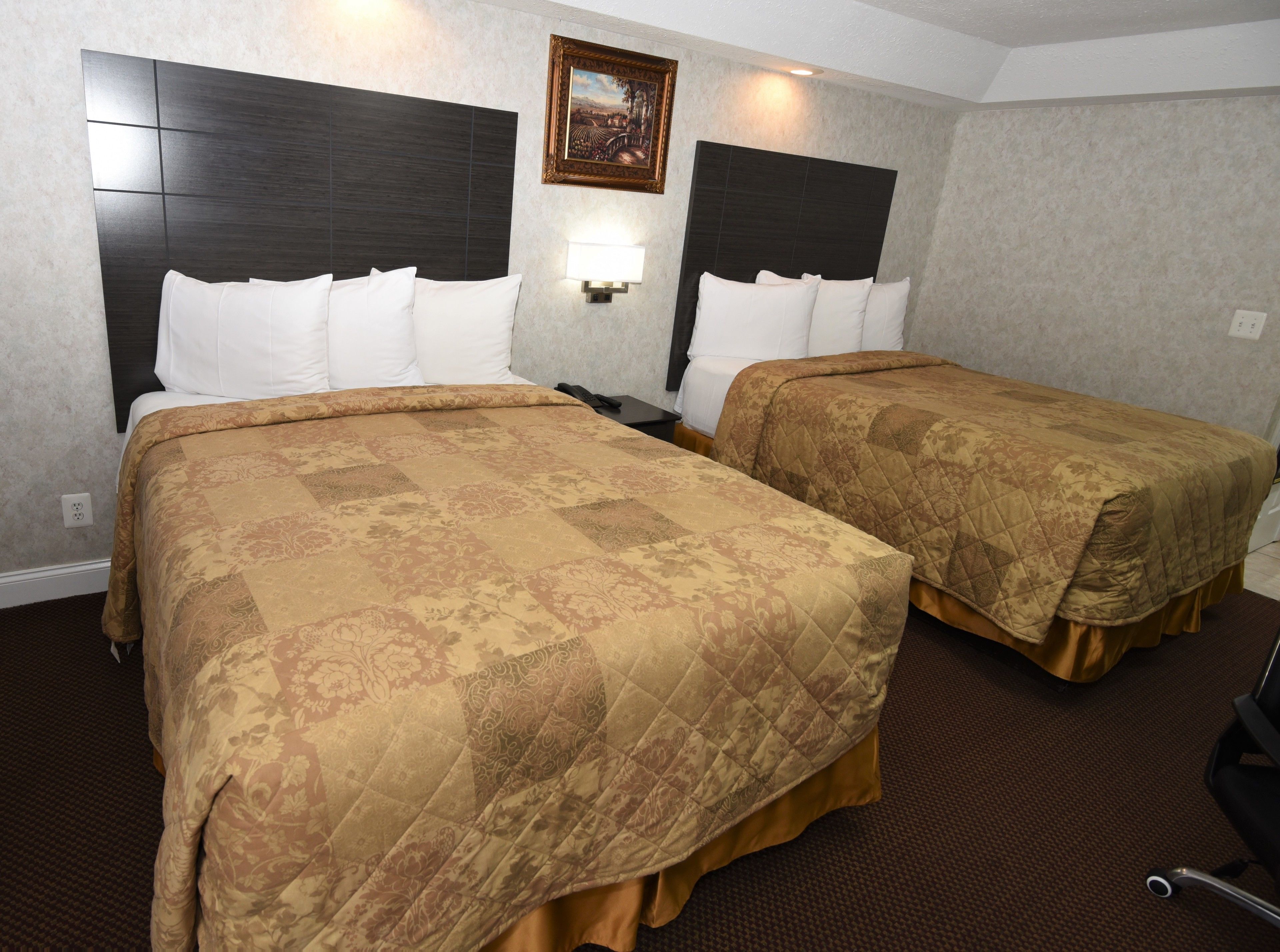 A hotel room with two beds, each with a headboard, a bedside table, and a lamp.