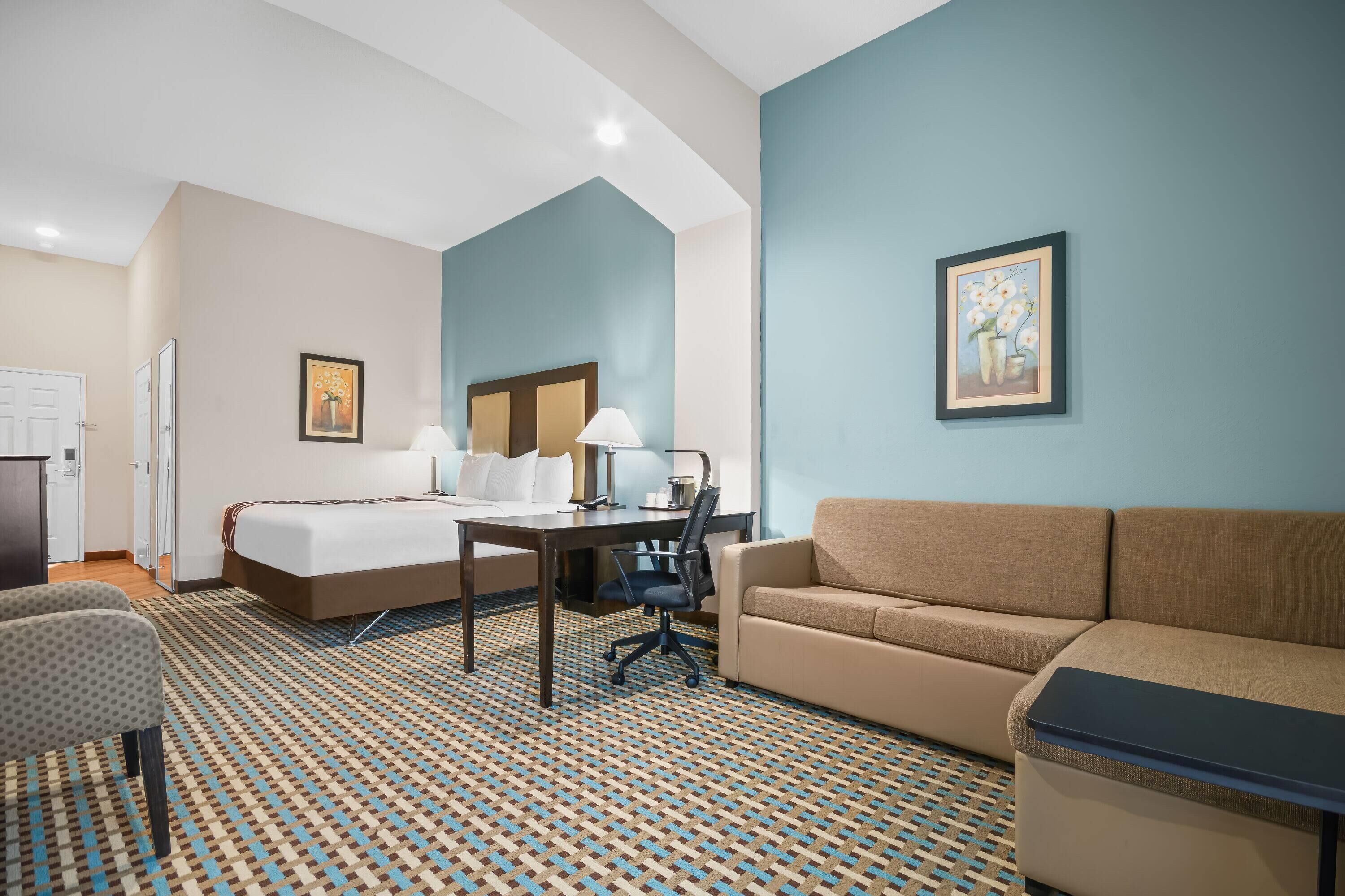 A hotel room with a bed, a desk, a chair, a sofa, and a patterned carpet.