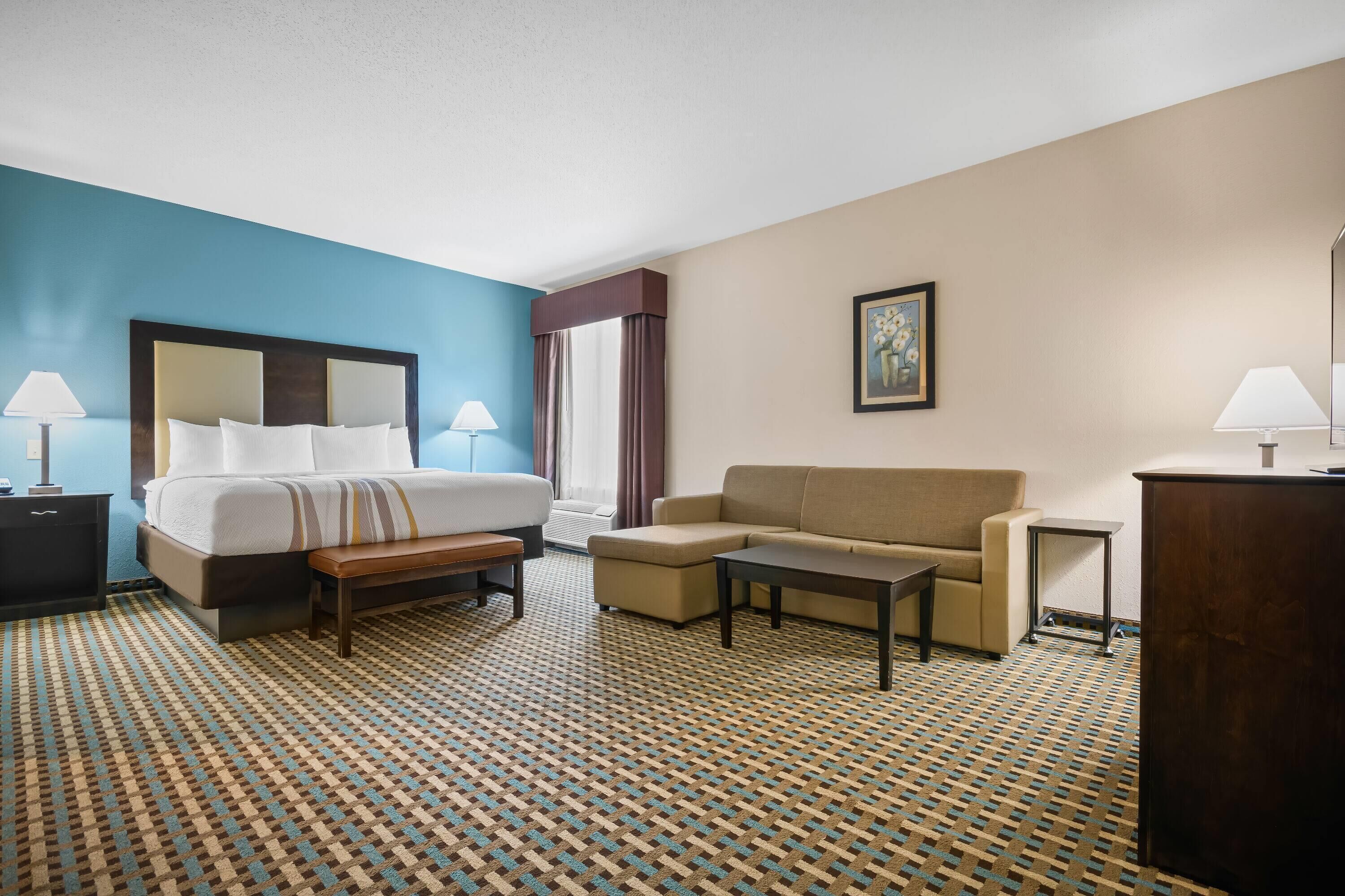 A hotel room with a bed, a sofa, a small table, a desk, and a patterned carpet.
