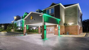 Un hotel con diseño moderno, que destaca por una entrada con marquesina iluminada en verde y un logotipo visible.