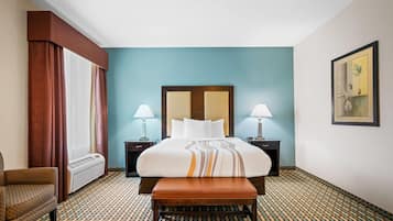 Una habitación de hotel con una cama, dos lámparas de noche, un banco, una silla y un suelo estampado.
